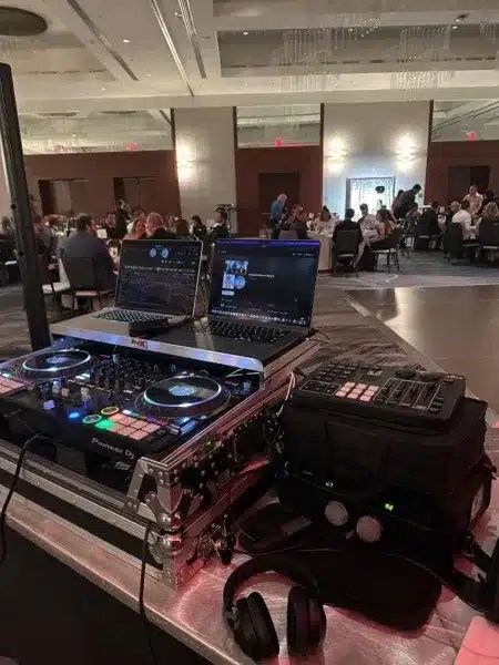 DJ booth with dual laptops, Pioneer controller, and headphones at a formal Grand Rapids Michigan event with seated guests.