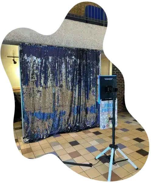 Indoor photo booth setup with blue and gold sequin backdrop and “FREE PHOTO” screen in Grand Rapids, MI.