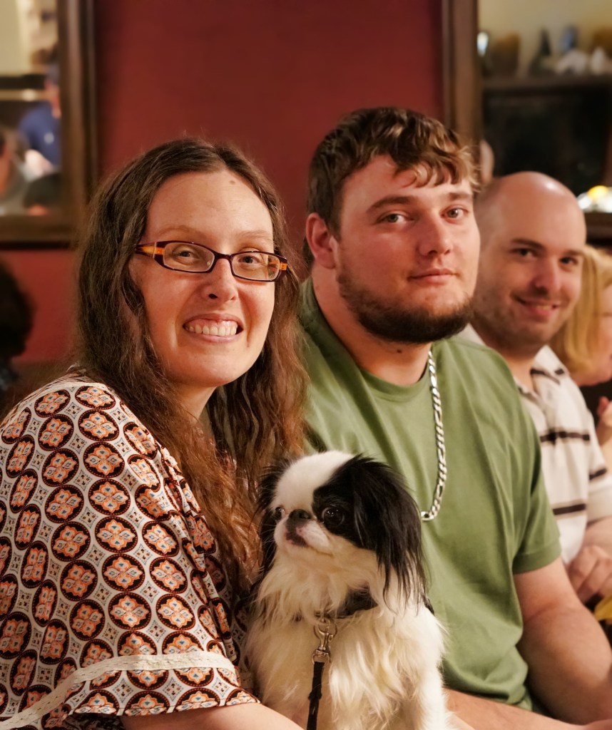 Veronica with Tommy.  Veronica is wearing a very 70s style shirt and Tommy has a green shirt on.  Hestia is on my lap, but not looking at the camera.