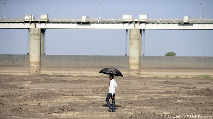 An Indian man holds an umbrella as he walks on the dry reservoir bed next to Gunda Dam in India's western Gujarat state, on April 1, 2016 (Getty Images/AFP/S. Panthaky)
