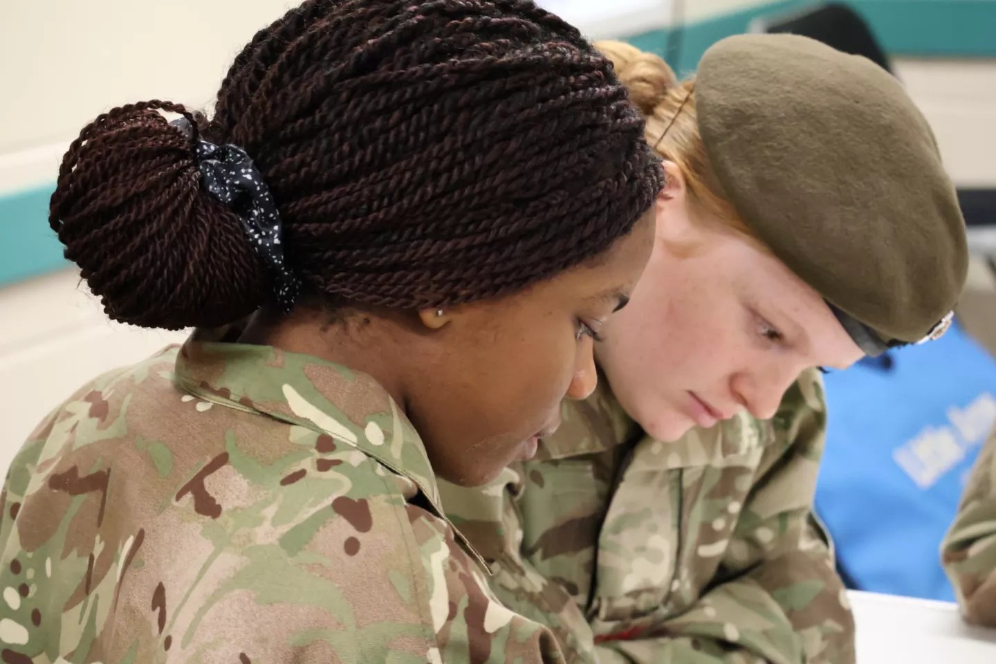 Two cadets wearing Army fatigues sit together at a desk, heads down as they study for their BTEC