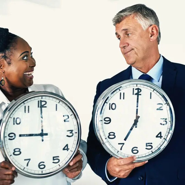 Two office workers holding up giant clocks