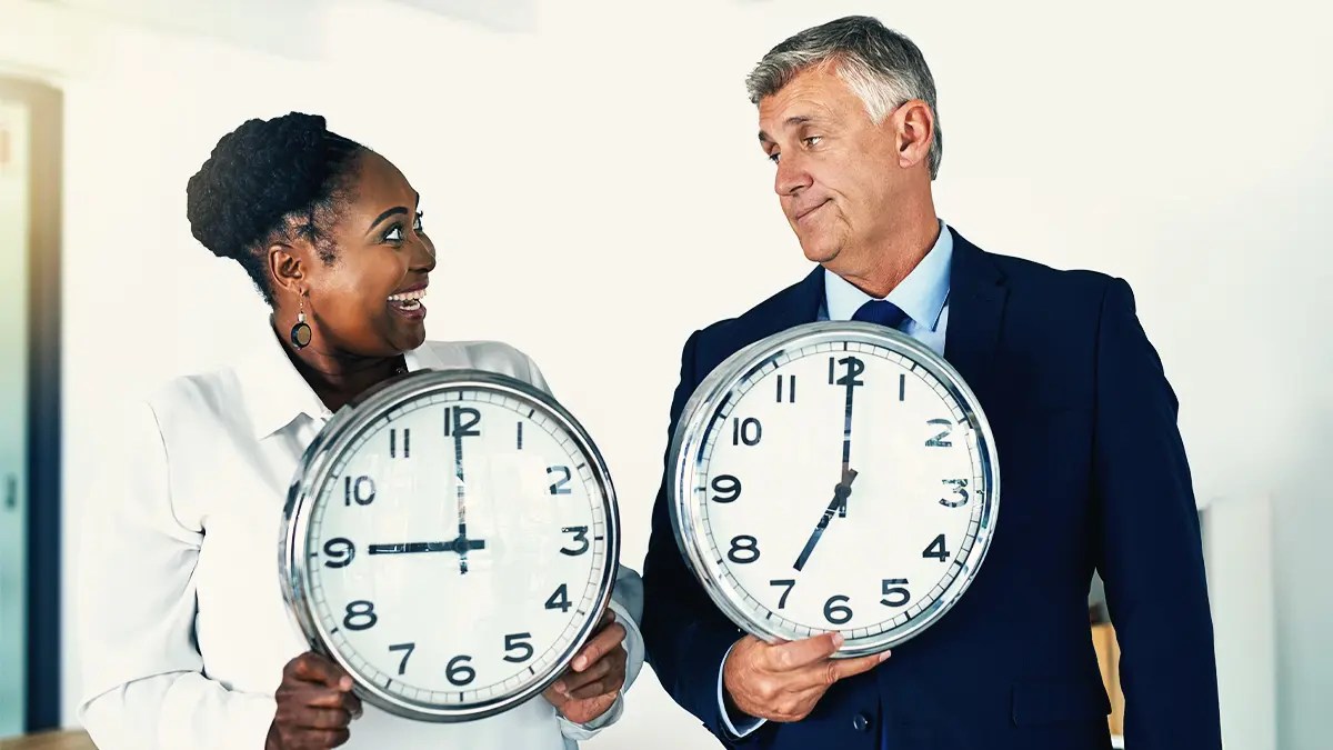 Two office workers holding up giant clocks