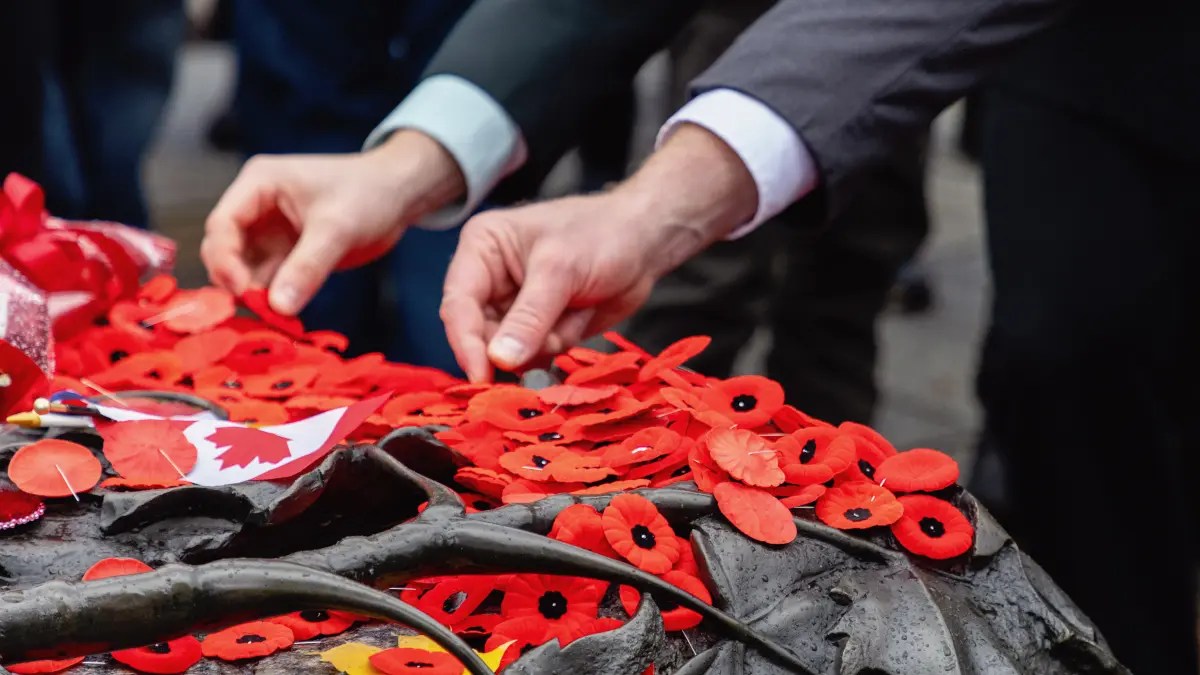 Image of men attending a remembrance day ceremony placing poppies across a war memorial