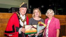 A man dressed in mayoral attire presenting an award to a woman
