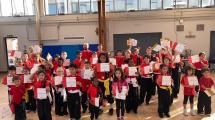 A large group of children in red and black holding medals and certificates