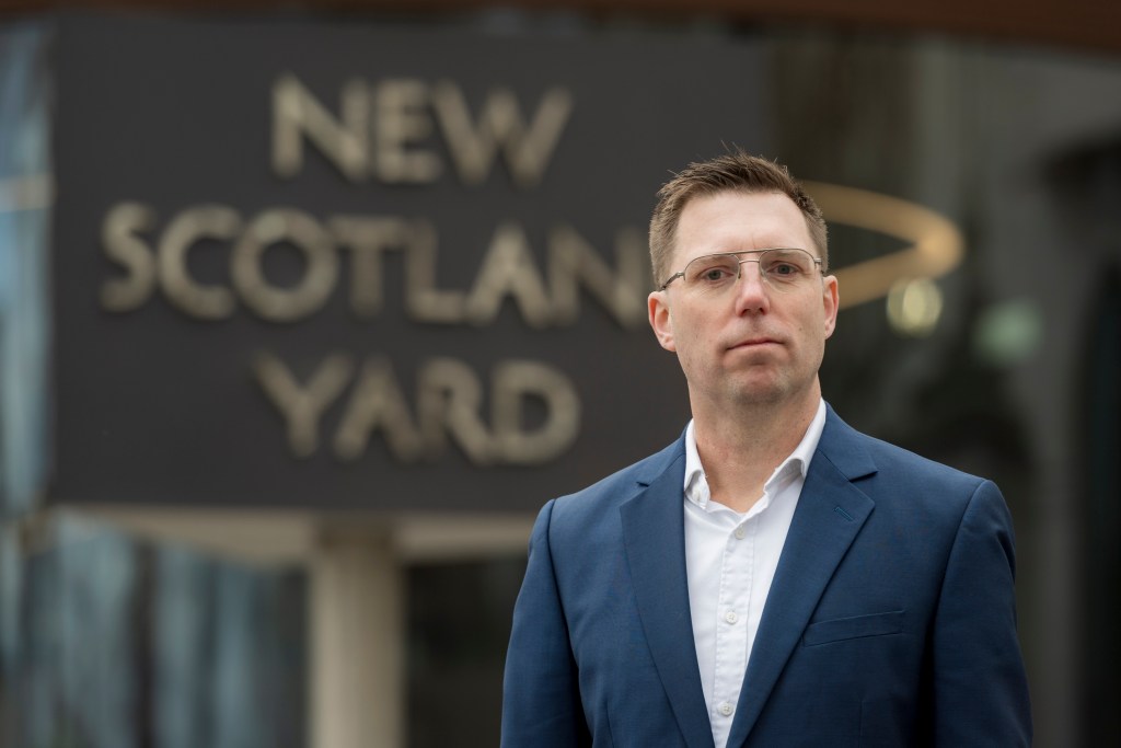 a man standing in front of the new scotland yard sign
