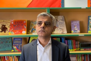 Sadiq Khan looking serious in front of a bookshelf with children's books
