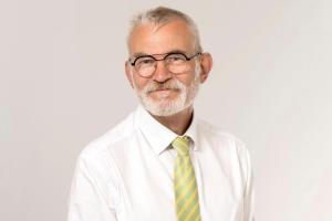 A man with a grey beard and glasses smiling