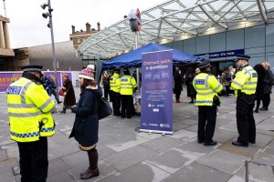 A police outreach event outside a train station, with officers engaging the public and a banner promoting safety.