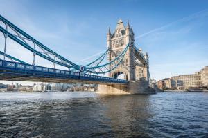 A view of Tower Bridge in London, showcasing its iconic blue and stone structure against a clear blue sky and the River Thames.