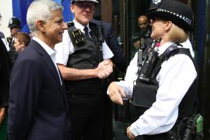 A man in a suit engages with two police officers outside a building, discussing matters while another officer watches on.