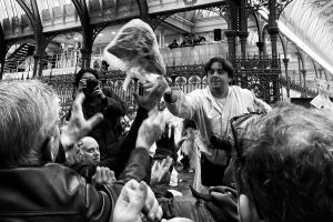 A bustling scene with people reaching out eagerly to receive items from a vendor amid a crowded market setting.