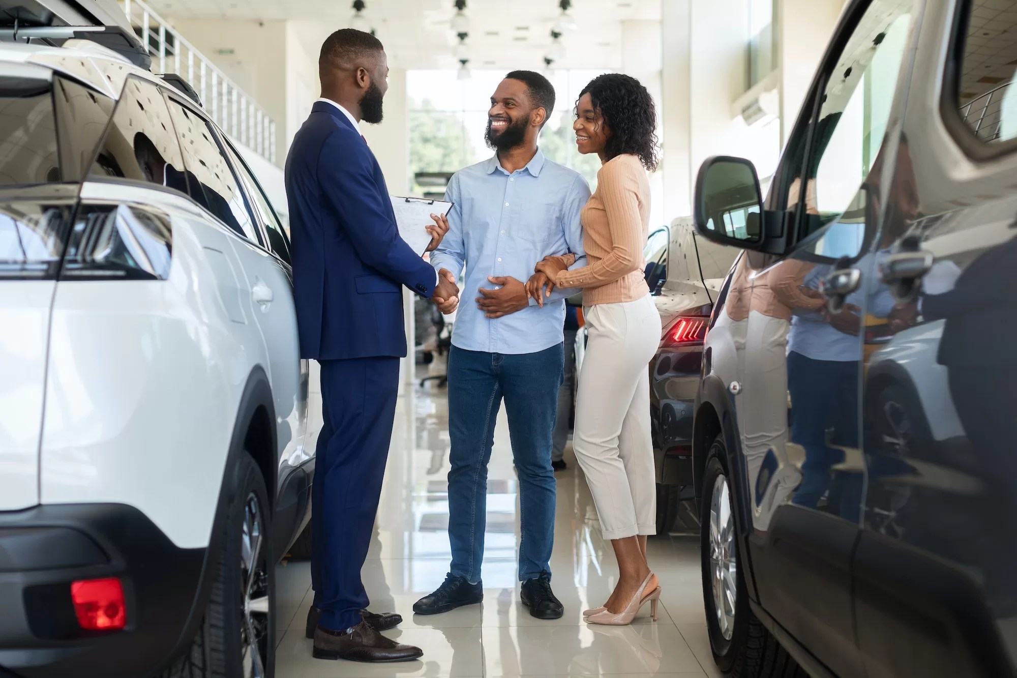 Car Purchase. Happy Customers Couple Handshaking With Manager In Auto Salon