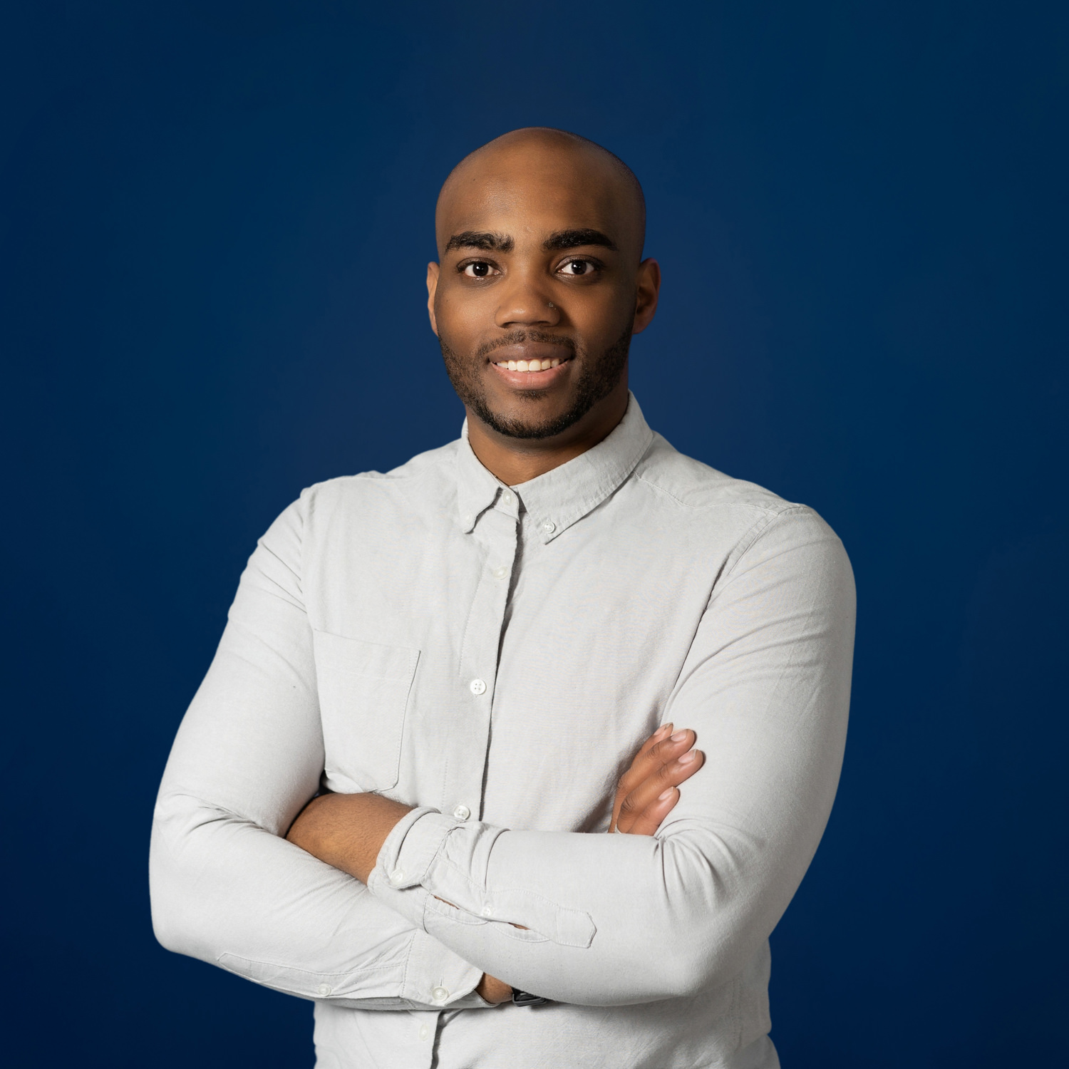 corporate headshot of a bald black guy with folded arms on a navy background
