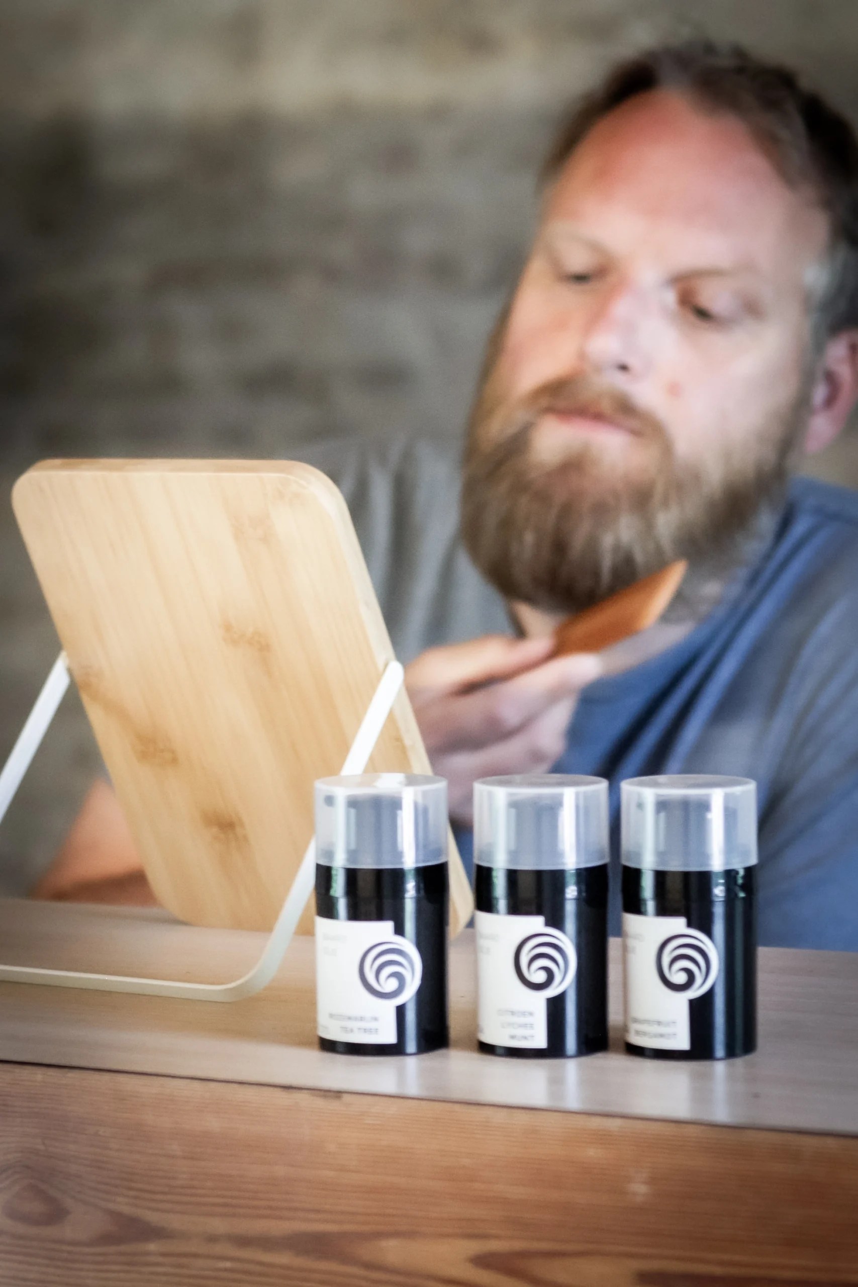 Man kamt zijn baard voor een spiegel, met drie flesjes baardolie die voor hem staan