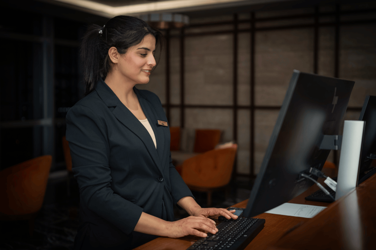 Wedding venue coordinator at a reception desk, scrolling through the venue website on a desktop computer to check where the enquiry form sits on the page