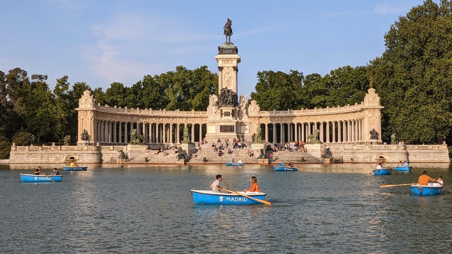 A couple in a small rowboat in a lake in front of a huge sculpture. Romantic things to do in Madrid