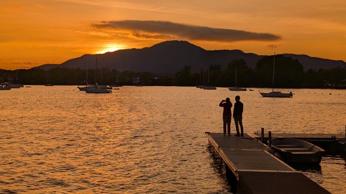 Sun going behind a mountain and two people standing on a deck admiring the sunset.
