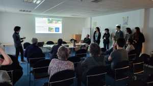 Young person standing at front of room presenting to group of seated people