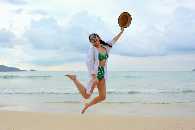 woman jumping on seashore and holding hat | what to wear in ibiza