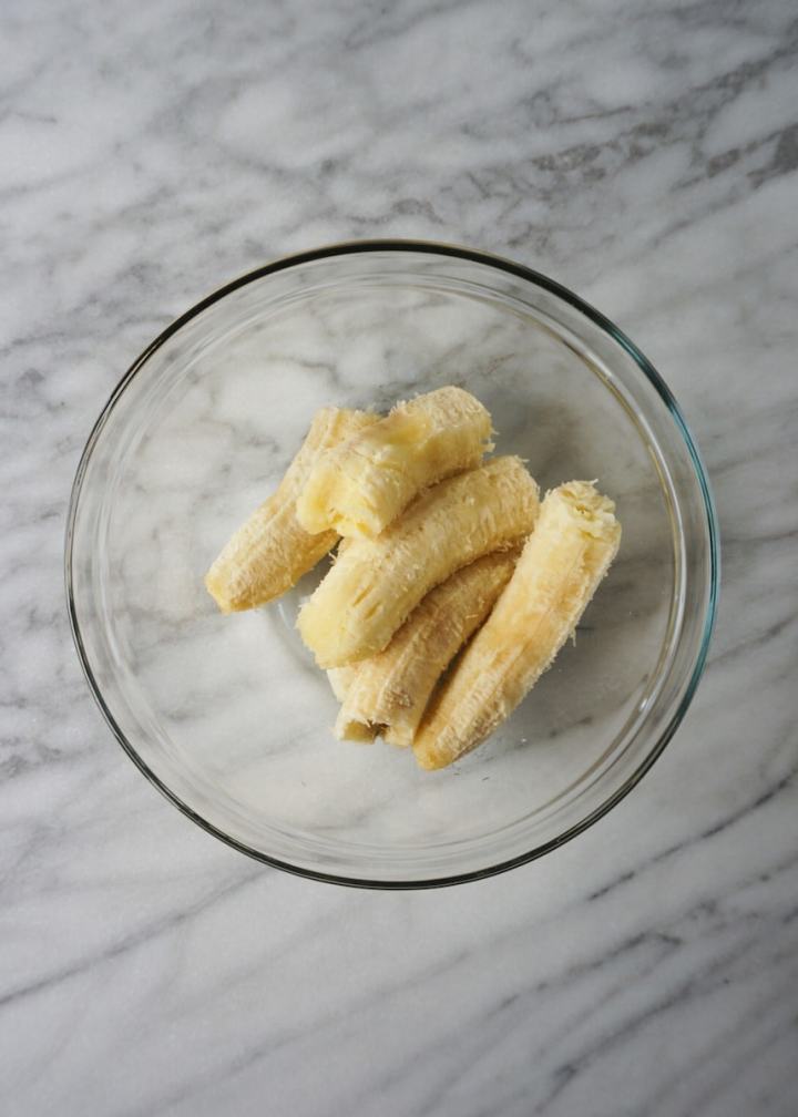 Bananas cut in half and placed in a clear glass mixing bowl.