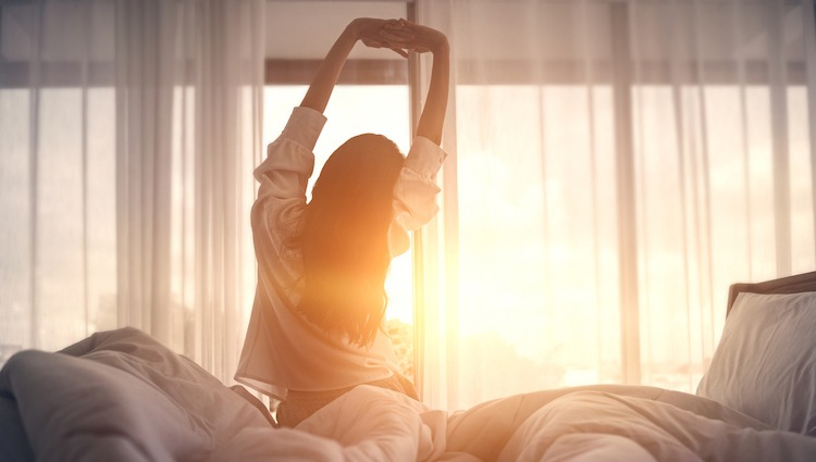 Happy woman stretching in bed after waking up. Happy young girl greets good day.