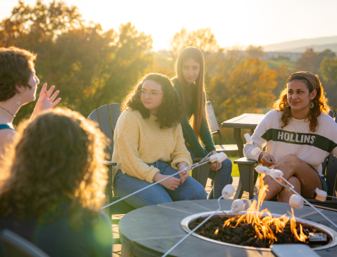 Students gather around a conversational firepit with mountains in the background.
