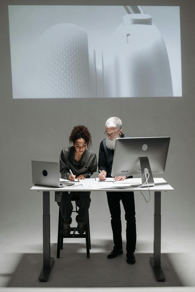 Two professionals collaborate in a high-tech setting with laptops and digital screens.