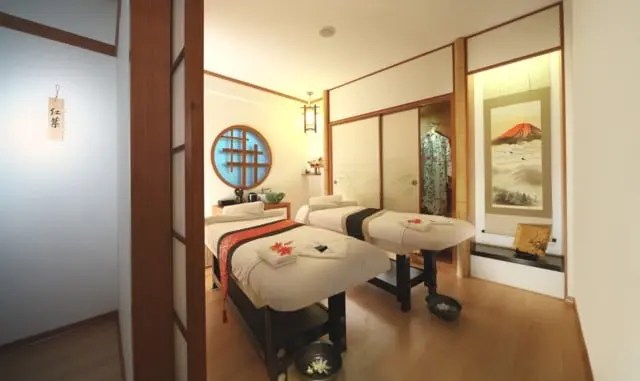 A Japanese-style massage room with two massage tables, folded towels, traditional decor, shoji screens, and a wall scroll featuring Mount Fuji.