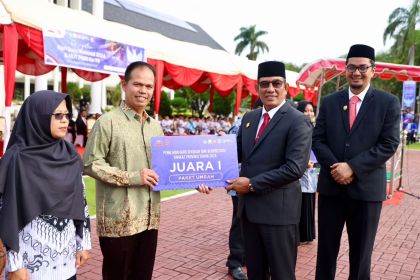 Plt. Sekda Aceh Muhammad Diwarsyah menyerahkan hadiah umrah kepada Guru dan Tendik (GTK) berprestasi, pada peringatan Hari Guru Nasional 2024 di halaman Kantor Gubernur Aceh, Kamis (5/12). (Foto: For Infoaceh.net)