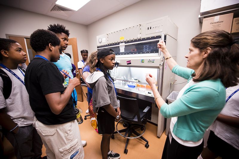 A group of young SciTech Institute participants listening to a scientist give a tour of her lab.