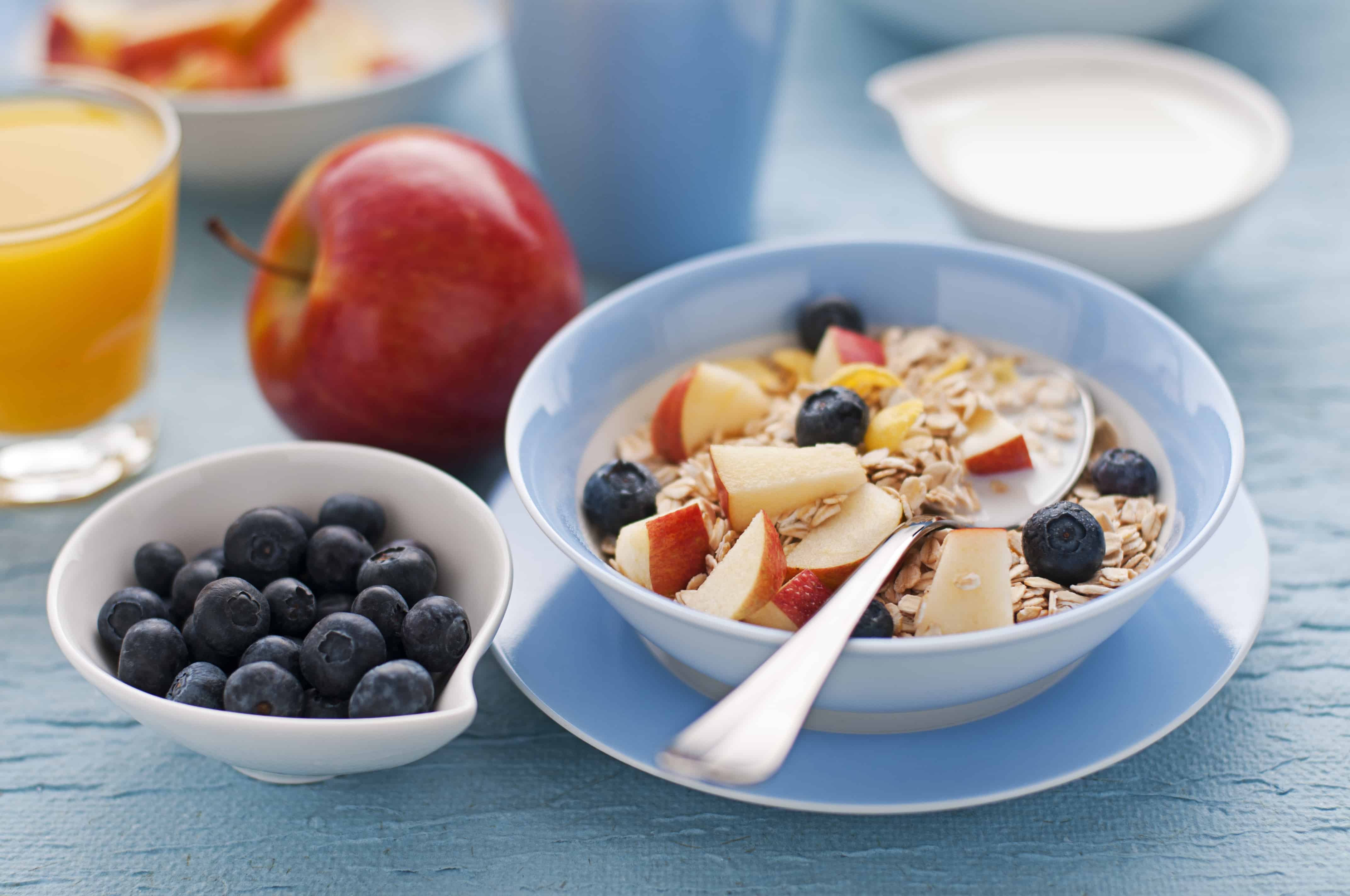 A bowl of oats covered in apple and blueberries with a glass of fresh orange juice