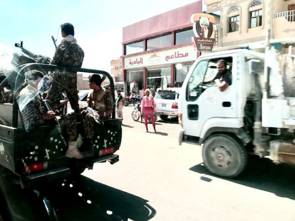 A truck with a large gun and three people in camouflage uniforms passes stores in Mareb, Yemen.