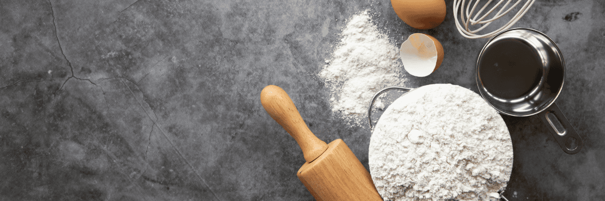 photo of flour, rolling pin, egg shell, whisk and measuring cup on a slate board