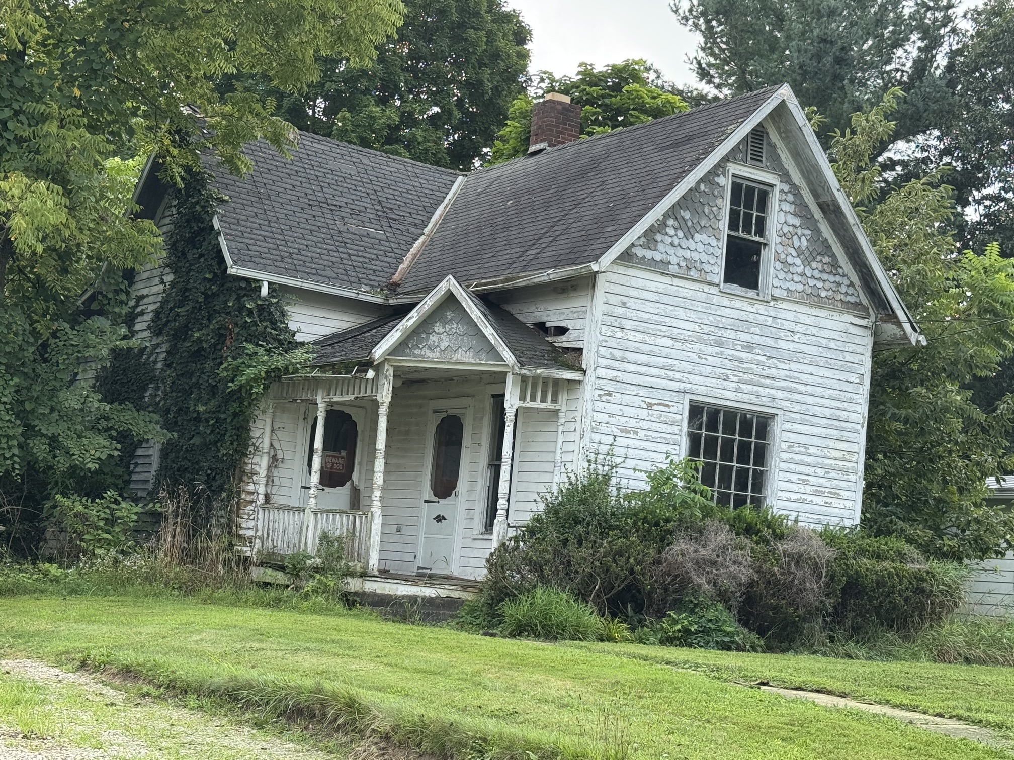 Dilapidated house with broken windows and overgrown weeds