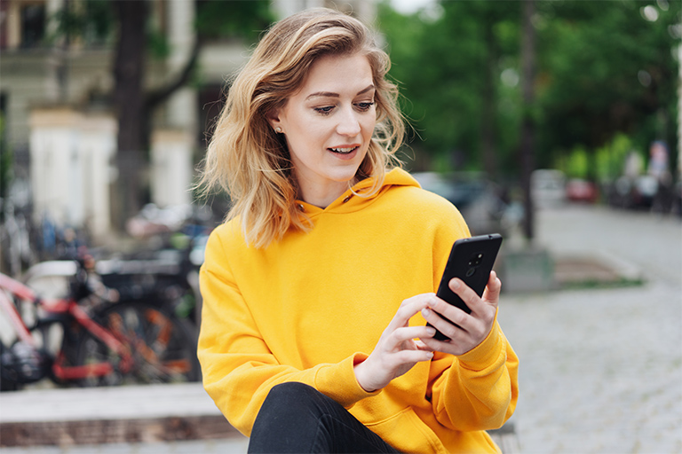 Eine junge Frau hält ein Smartphone in der Hand.