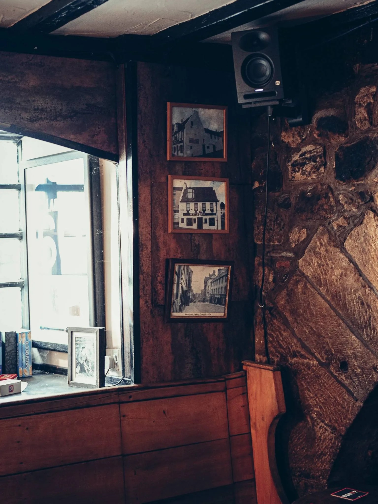 Coin de bois et de pierre du Settle Inn, a Stirling, avec des photos anciennes au mur et une enceinte, dans la lumiere tamisee du pub.