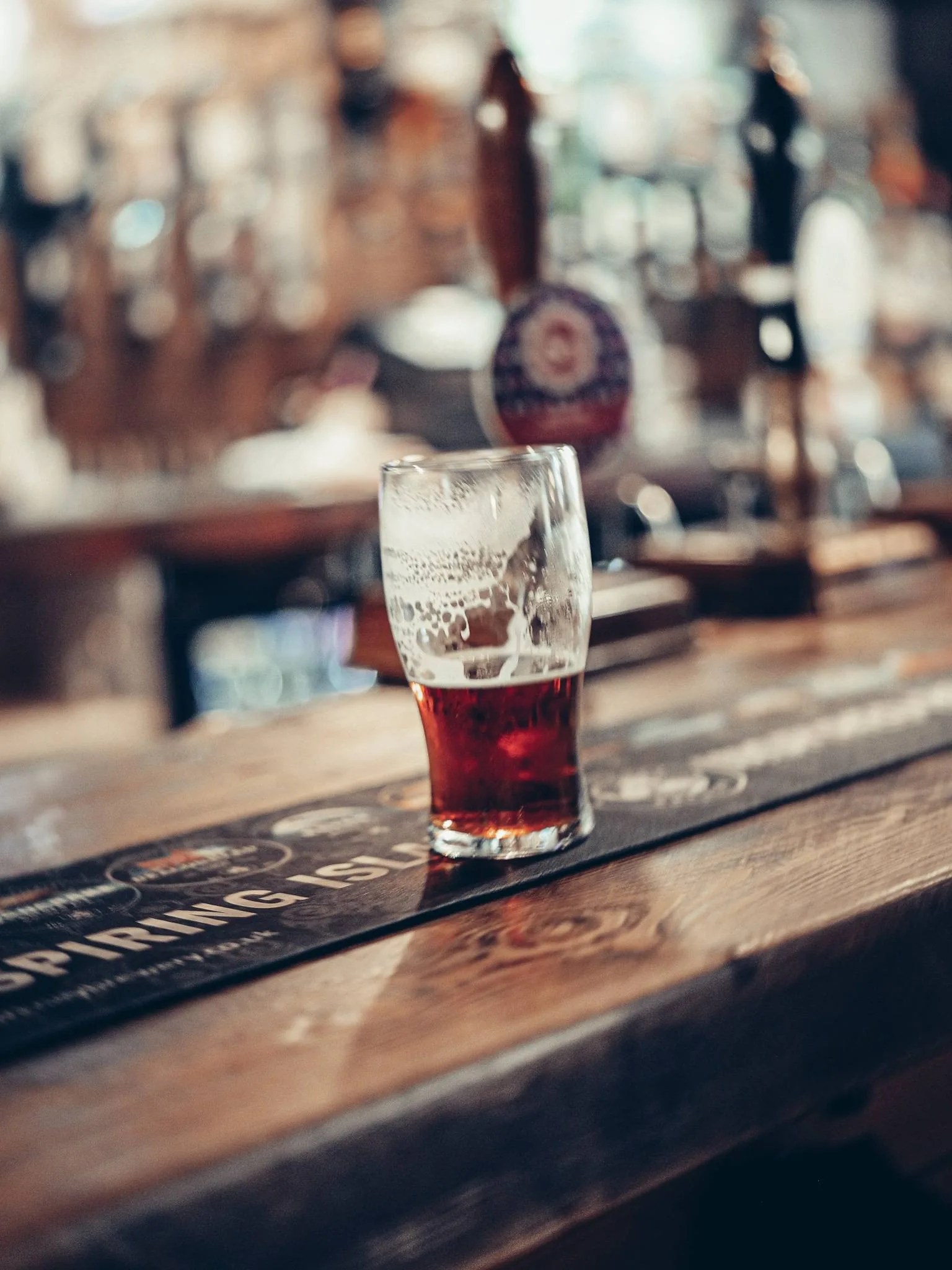 Un demi de biere ambree sur le comptoir de bois du Settle Inn, a Stirling, les pompes a biere en arriere-plan.