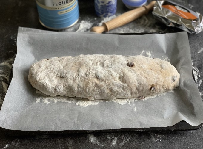 After half an hour, roll the marzipan out to make a long flat sausage shape that fits inside the stollen dough. Place the marzipan in the middle of the dough and roll it up to make a large roll shape, making sure the sealed side is underneath.