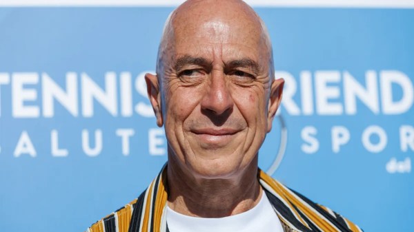 L’attore italiano Roberto Ciufoli sorride davanti a un cartellone blu durante un evento sportivo, dopo aver superato un intervento per cancro renale.