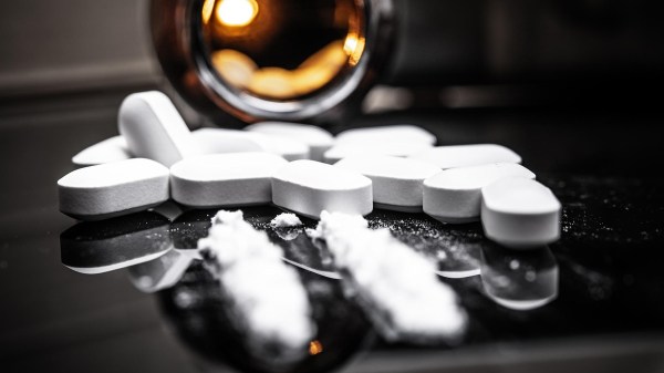 Compresse bianche sparse su una superficie nera accanto a un barattolo aperto, con polvere bianca in primo piano, simbolo di abuso di farmaci o sostanze.