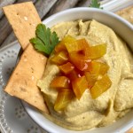 Overhead view of golden beet hummus in a white bowl with flatbread crackers garnished with chopped beets and parsley