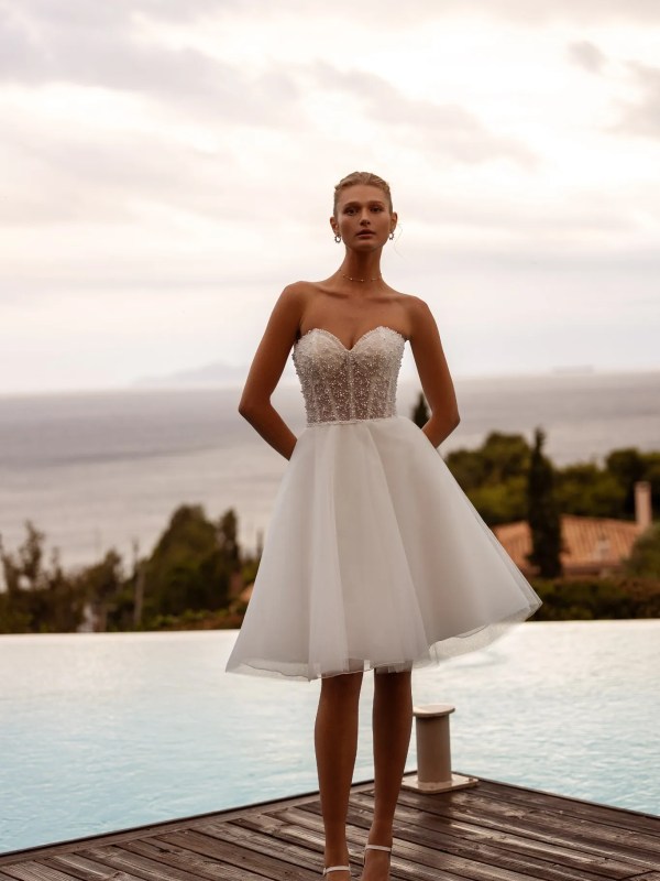 Robe de mariée courte bustier DR411 devant une piscine, vue de face