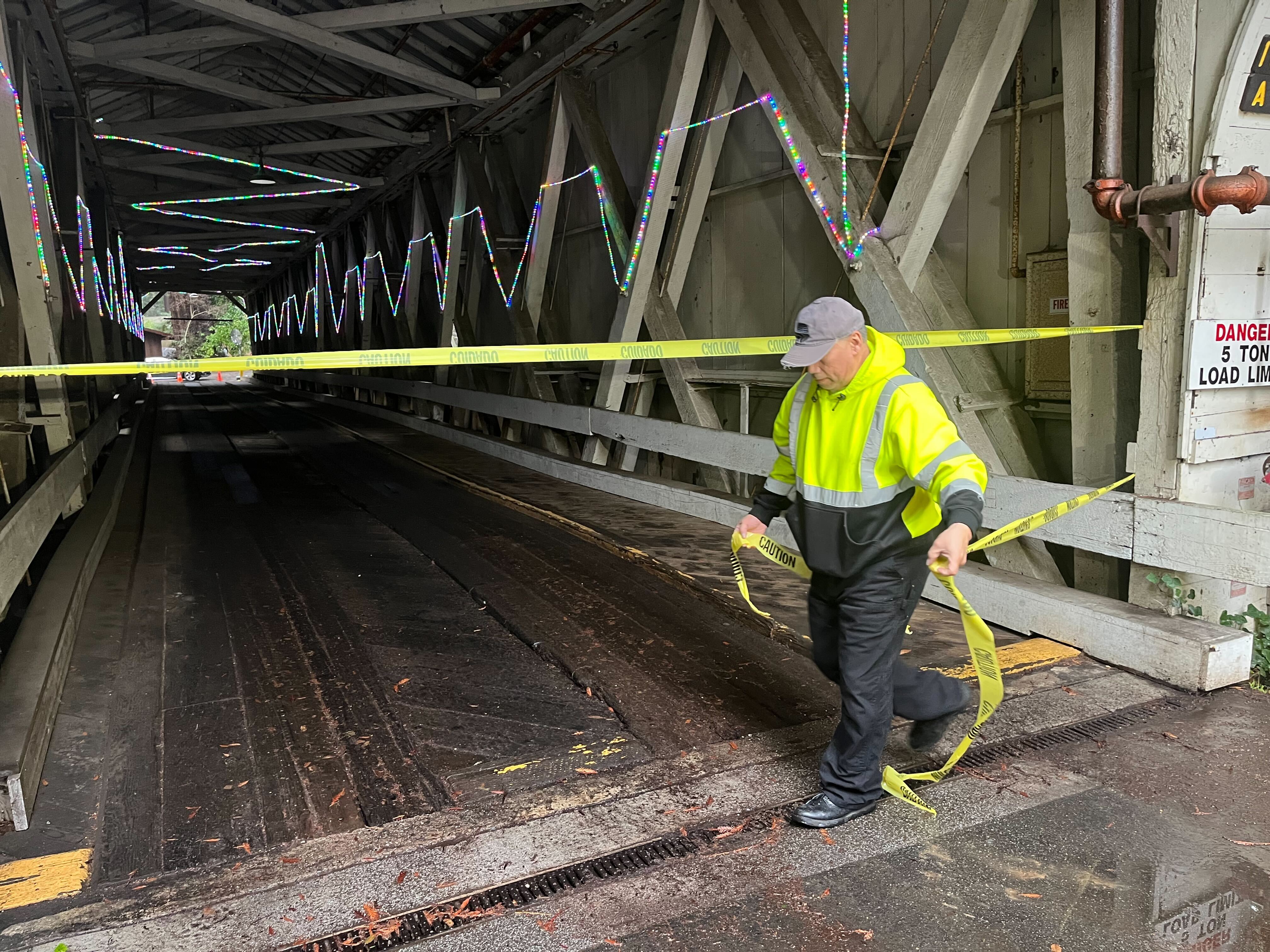 Paradise Park maintenance chief Andrew Almonza tapes off a covered bridge and its missing post in unincorporated Santa Cruz County, Calif., on Monday, January 9, 2023. (Ethan Baron/Bay Area News Group)