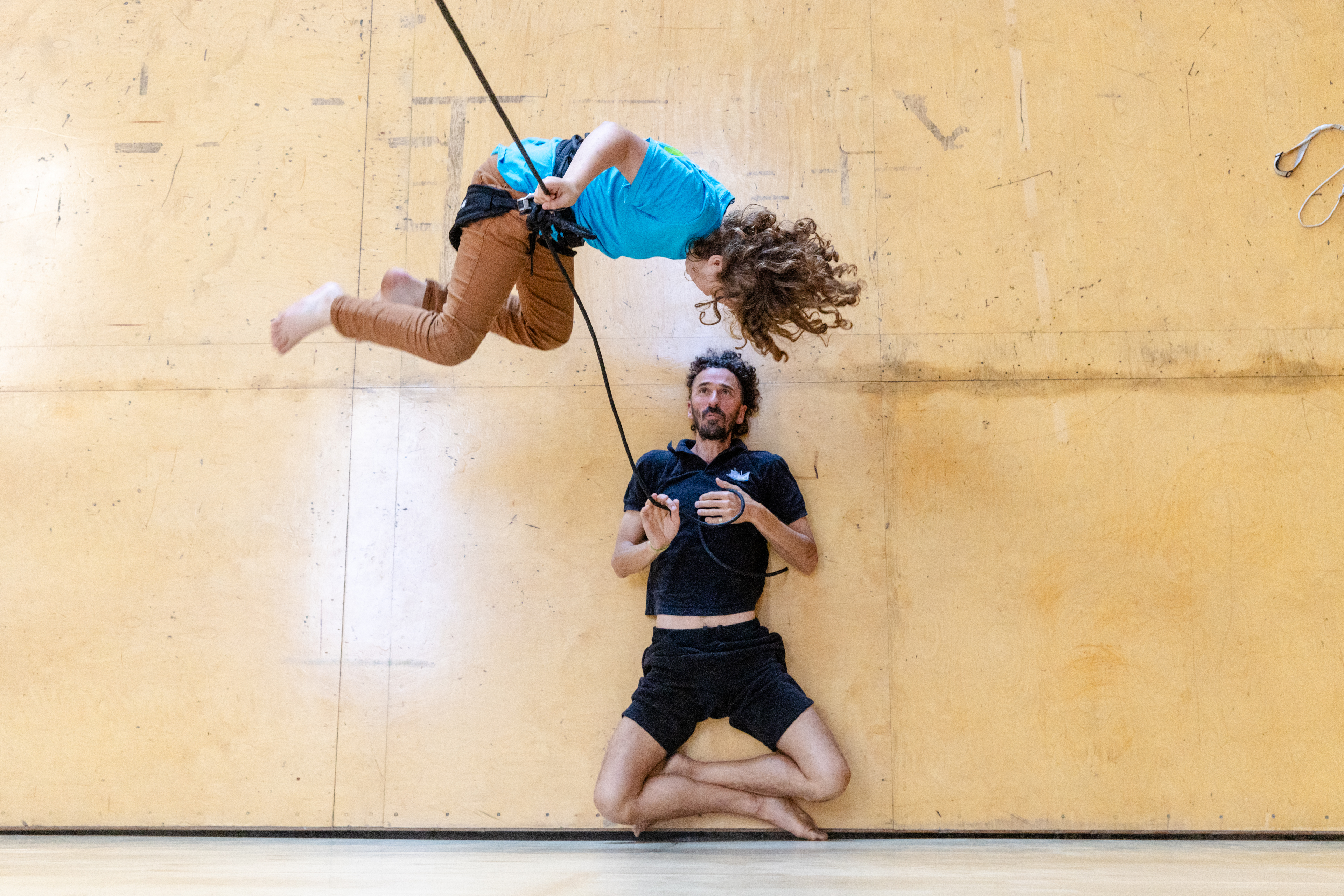 OAKLAND, CA - NOVEMBER 12: Student Arlo Dean of Oakland (left) performs arial maneuvers while hanging in the air from a rope attached to a harness while instructor Roel Seeber holds the rope while laying on the floor during a flight test vertical dance lesson at the BANDALOOP open house at their studio space in Oakland, Calif. on Nov. 12, 2023. BANDALOOP is a renown vertical dance troupe, that have performed their aerial mid-air performances on international landmarks around the world. (Douglas Zimmerman/Special to the Bay Area News Group)