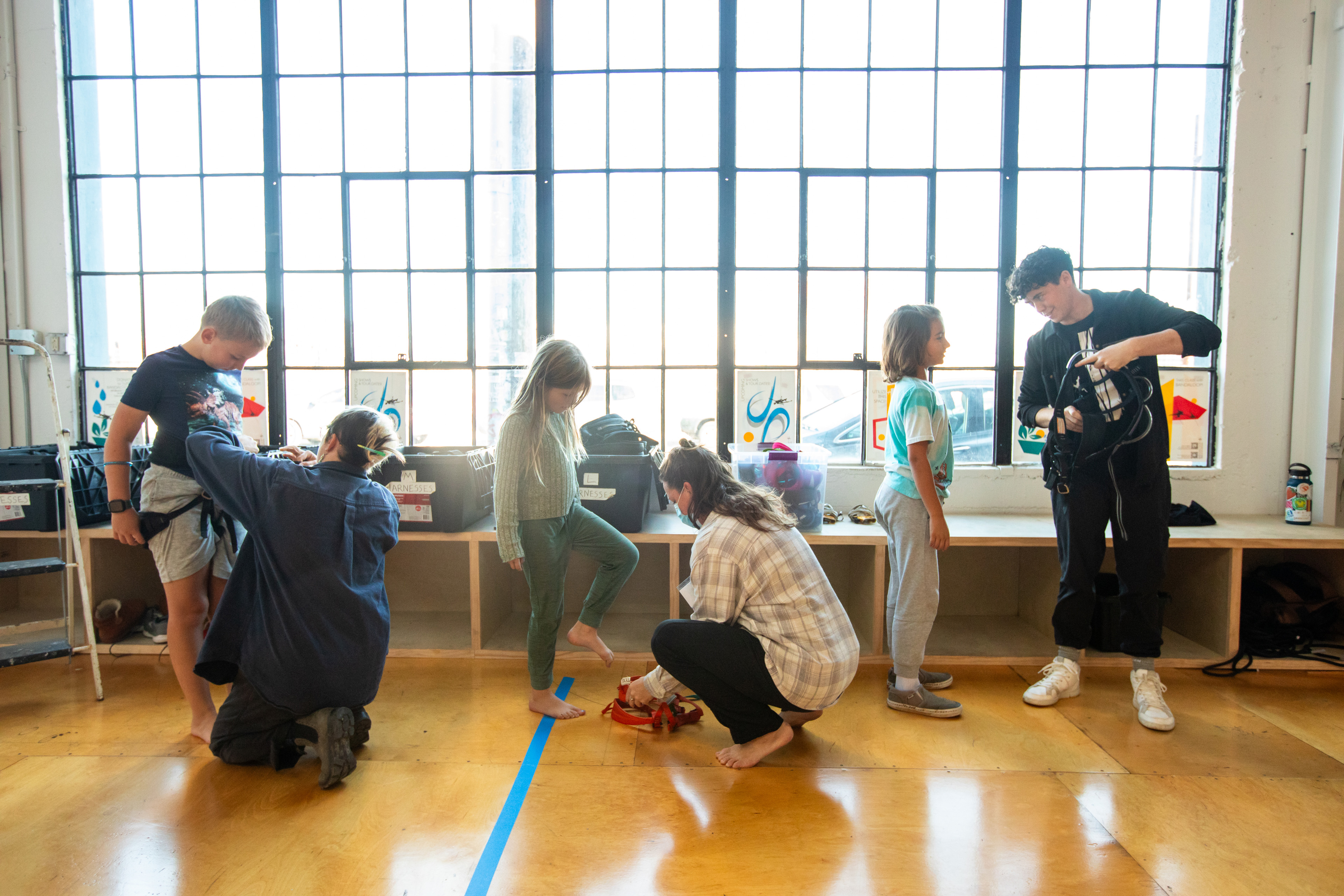 OAKLAND, CA - NOVEMBER 12: (Left to right) Elliot Smith has a harness put on by instructor Krystal Harfert, while Avery Smith has a harness put on by instructor Sarah Keeney and Memo Rehberg is shown how to wear a harness from instructor Becca Dean before flight test vertical dance lessons at the BANDALOOP open house at their studio space in Oakland, Calif. on Nov. 12, 2023. BANDALOOP is a renown vertical dance troupe, that have performed their aerial mid-air performances on international landmarks around the world. (Douglas Zimmerman/Special to the Bay Area News Group)