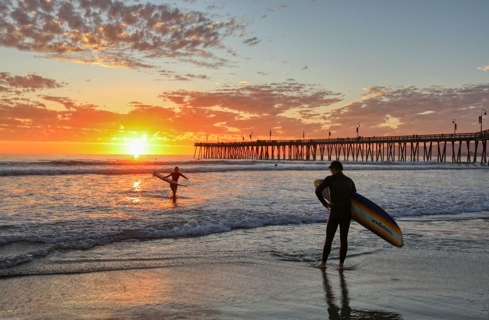 Os surfistas veem o sol se afogando no Oceano Pacífico em Pismo Beach. 