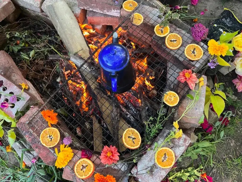 feu de camp avec une bouilloire sur les flammes entourées de fleurs et de morceaux d'orange