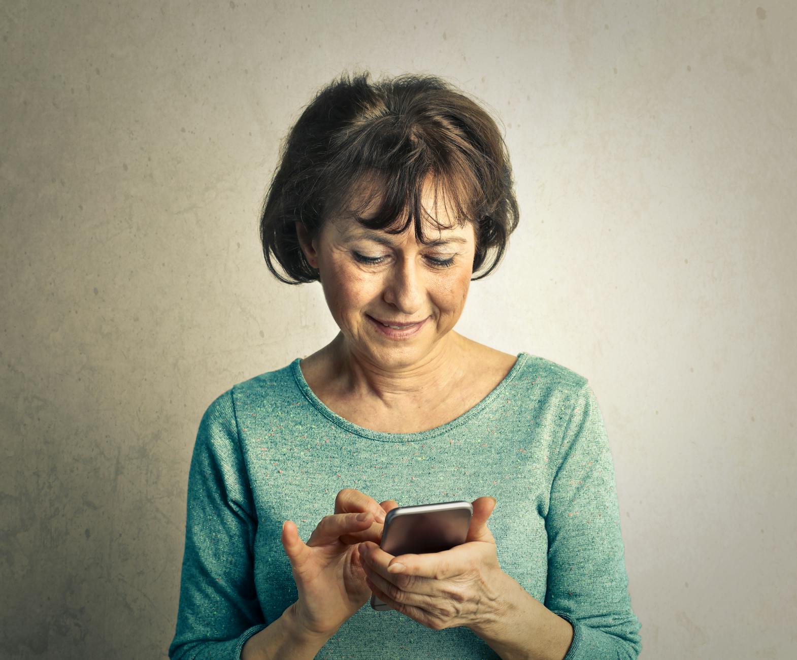 elderly woman in green long sleeve shirt is having fun using smartphone